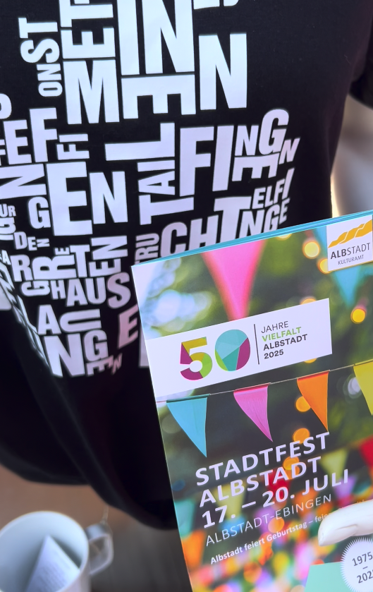 Der Buchstabenort Albstadt als Shirt neben dem Jubiläumsflyer zum 50-jährigen Stadtjubiläum